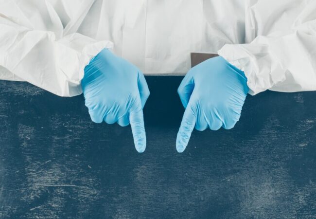 doctor-mask-gloves-protective-suit-pointing-down-looking-white-dark-placard